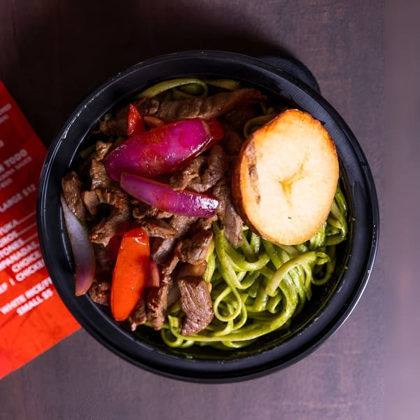 Peruvian Lomo Saltado with green noodles, beef, red onions, peppers, and a fried plantain slice.