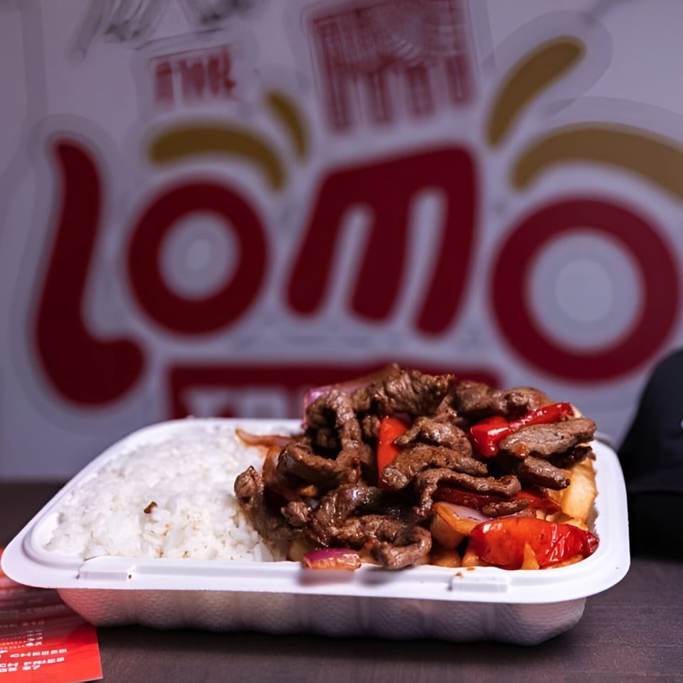 Lomo Saltado with rice in a takeout container, with the Lomo Truck logo blurred in the background.