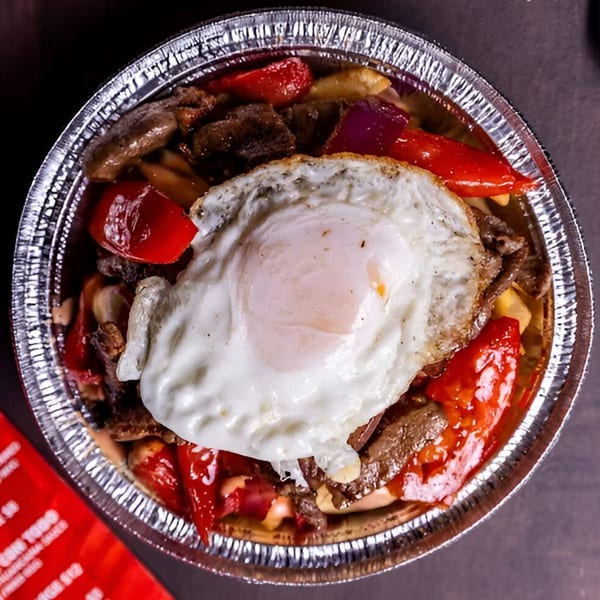 Peruvian Lomo Saltado with steak, red peppers, onions, and a fried egg in a foil container.