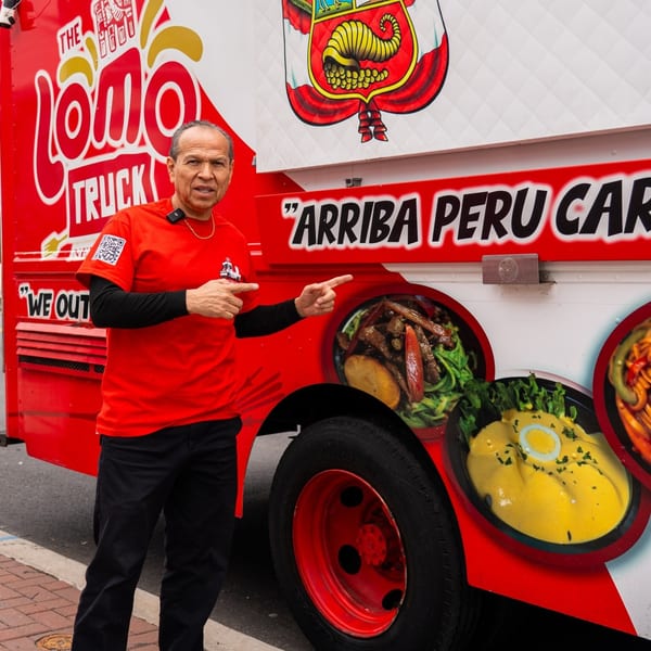 Man in red Lomo Truck shirt pointing at Peruvian food images on the side of a food truck.