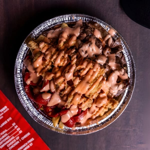 Peruvian Lomo Saltado in a foil container, topped with creamy sauce, chicken, beef, and red peppers.