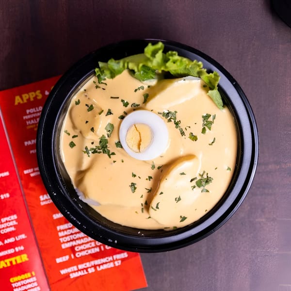 Peruvian Papa a la Huancaína, yellow sauce over potatoes, garnished with lettuce, parsley, and a hard-boiled egg.