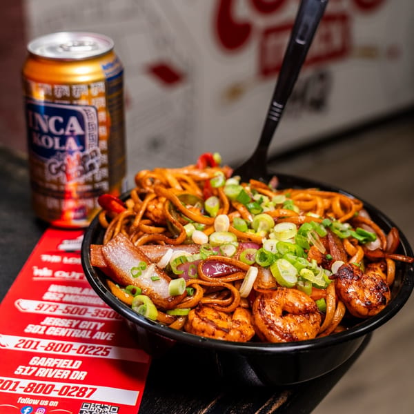 Peruvian Lomo Saltado noodles with shrimp, onions, and scallions, next to an Inca Kola can.