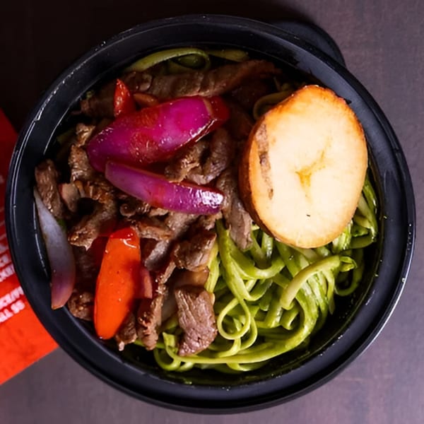 Peruvian Lomo Saltado with green noodles, beef, red onions, and a fried plantain slice.