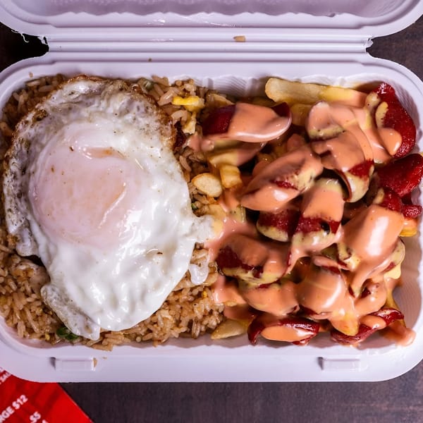 Peruvian Lomo Saltado with fried rice and a sunny-side-up egg in a white takeout container.